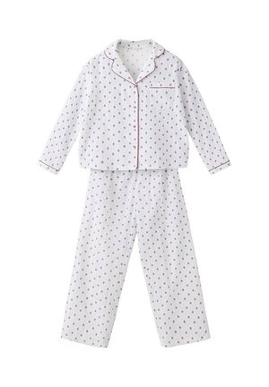 Mujer con pijama blanco de manga larga con estampado, con detalles rojos y zapatillas marrones, de pie frente a un fondo blanco liso.