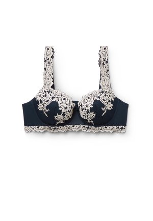 Tmavě modrá podprsenka s kosticemi s bílým květinovým krajkovým potahem na košíčcích, ramínkách a spodním okraji, zobrazena na bílém pozadí.