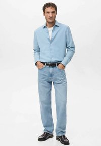 Camisa de botones azul claro, camiseta blanca debajo, jeans azul claro, cinturón negro y zapatos negros brillantes. Diseño sencillo y ajuste relajado.