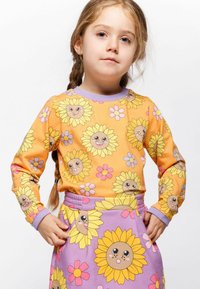 Langärmliges Oberteil und Rockset in Orange und Lila, mit Sonnenblumenmotiven mit lächelnden Gesichtern und floralen Akzenten auf weichem Stoff.