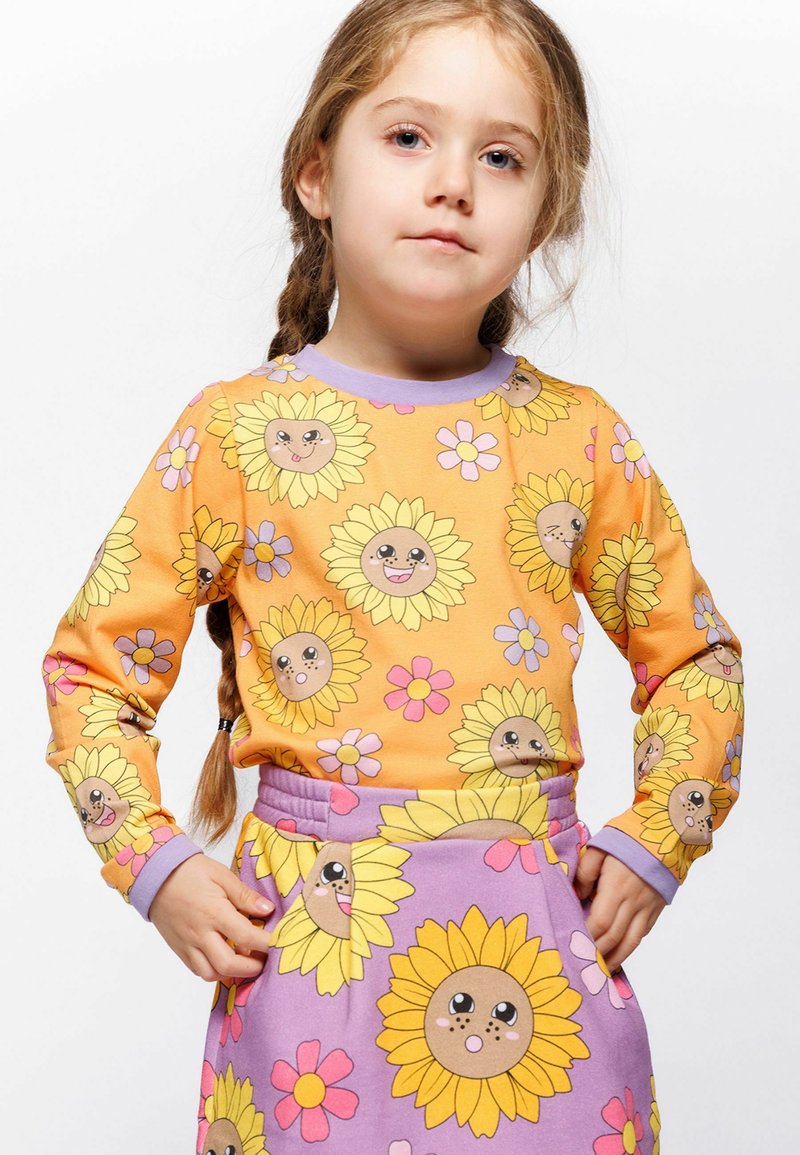 Langärmliges Oberteil und Rockset in Orange und Lila, mit Sonnenblumenmotiven mit lächelnden Gesichtern und floralen Akzenten auf weichem Stoff.