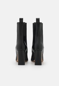 Botas de tobillo de cuero negro con un acabado elegante y suave, tacón cuadrado, costuras laterales y tiradores en la parte posterior para facilitar su uso.