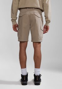 Beige cargo šortky s bočními kapsami, nastavitelným pasem a volným střihem. Nosené s černými teniskami a bílými ponožkami do pírek.