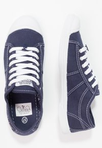 Sneakers in tela navy con lacci bianchi e punte in gomma. La cucitura bianca accentua il design. L'interno presenta una soletta decorata.
