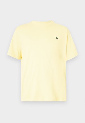 T-shirt de algodão amarelo com mangas curtas, gola redonda e um pequeno logotipo verde bordado no lado esquerdo do peito. Textura suave e corte descontraído.