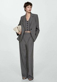 Gray pinstripe suit with a cropped blazer, matching high-waisted trousers, and a sleeveless top featuring black buttons. Holding a beige clutch.