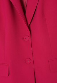 Fuchsiový blazer s dvěma kulatými knoflíky, s klopovém límcem a předními kapsami. Hladká tkanina s přiléhavým střihem a jemnými švy.