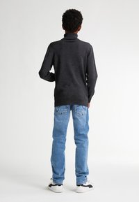 Schwarzer Rollkragenpullover mit einem strukturierten Strickdesign, kombiniert mit hellblauen Jeans und weißen Sneakers mit schwarzen Akzenten.