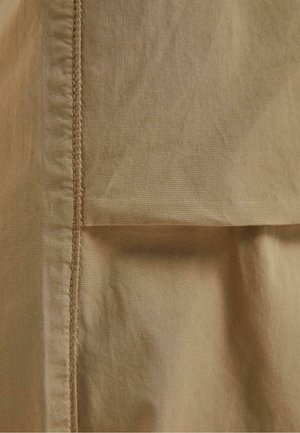 Pamukasti materijal u mekoj bež boji s vidljivim šavovima. Ima glatku teksturu i detalj s presavijenim rubom.