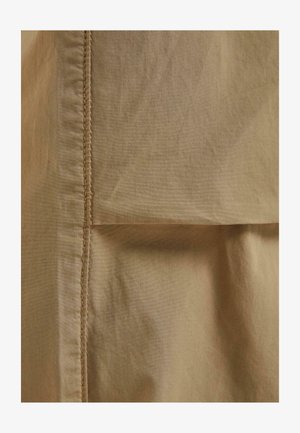 Bavlnená tkanina v jemnej béžovej farbe s viditeľným šitím. Disponuje hladkou textúrou a detailom preloženého okraja.