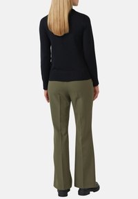 Zwarte gebreide trui met geribde zoom, gecombineerd met olijfgroene pantalon. Soepele textuur, rechtmodel, enkel-lang, en zwarte schoenen.