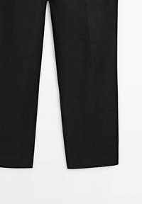 Pantalons noirs à jambes droites, visibles de la mi-cuisse à l'ourlet sur un fond blanc.