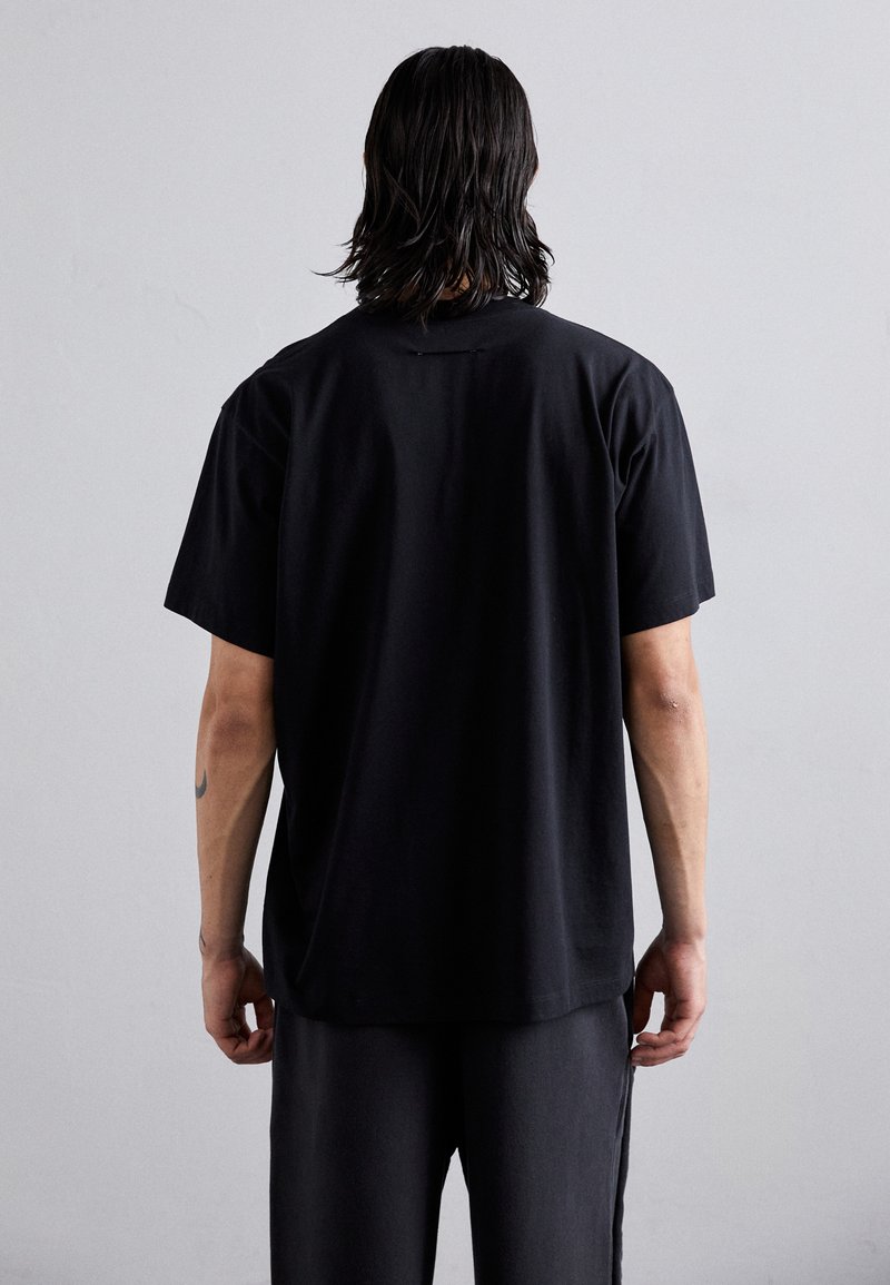 T-shirt nera a maniche corte in cotone, con vestibilità rilassata e orlo arrotondato, caratterizzata da una texture liscia e da un design semplice.