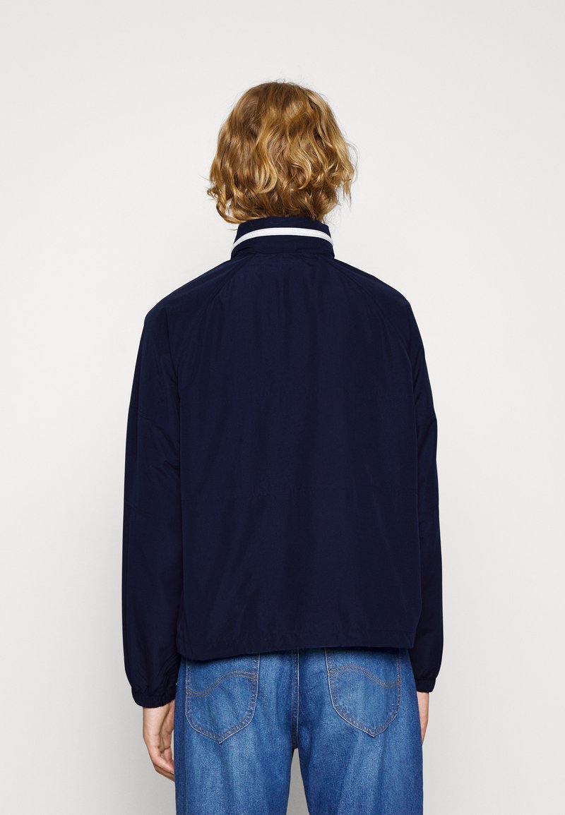 Giacca blu navy con colletto alto, polsini elastici e design aerodinamico. Realizzata in un tessuto liscio, presenta dettagli di colletto a contrasto.