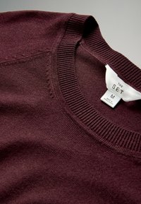 Burgundy pulóver bordás kerek nyakkal és sima textúrával. A címke "THE SET" feliratú, M-es méretű, és "Bangladesben készült" felirattal.