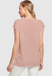 Lys pink kortærmet T-shirt med en blød tekstur og en lidt løs pasform. Ryggen har en rund halsudskæring og opsmøgede ærmer.