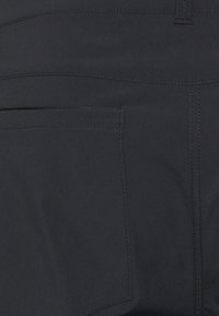 Pantalon en tissu noir avec une texture lisse, une couture de poche courbée et une poche zippée, avec des coutures droites le long des bords.