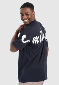 Námořnická modrá bavlněná tričko s krátkým rukávem, na zádech s velkým bílým nápisem "smile". Klasický design s kulatým výstřihem, měkká textura.