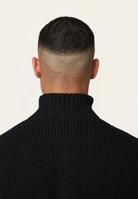 Schwarzer ribbeliger Strickpullover mit hohem Kragen, der ein strukturiertes Design und eine glatte Rückseite aufweist. Der Ausschnitt ist schmal und gut geformt.