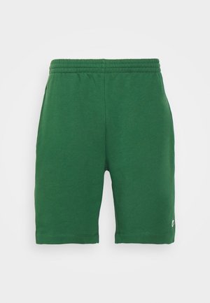 Grüne knielange Shorts mit elastischem Bund und kleinem weißem Logo nahe dem unteren Saum auf einfarbigem Hintergrund.
