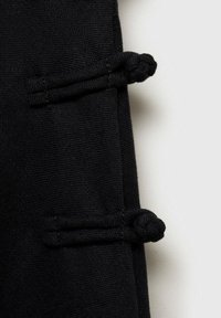 Schwarzer Stoff mit strukturierter Oberfläche, der durch zwei Knotenakzente und gestickte Details Tiefe und Struktur in das Design bringt.
