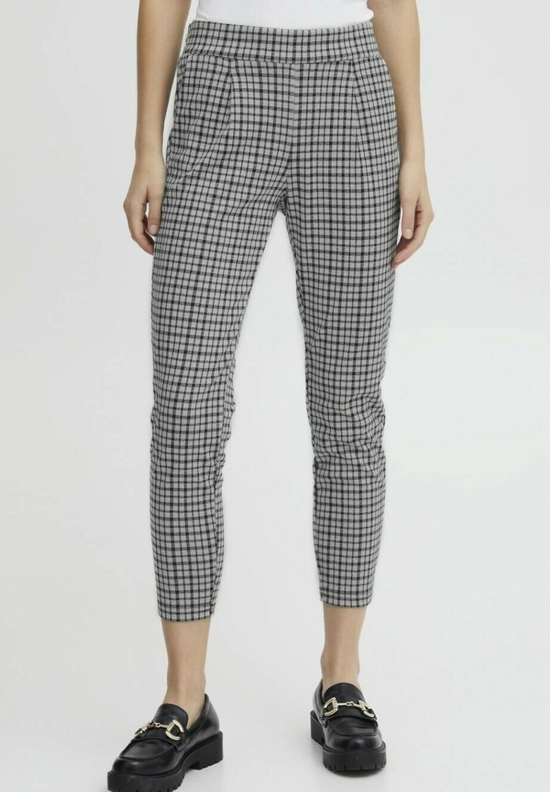Pantaloni a quadri grigi e neri con un design aderente, dotati di vita e pieghe, abbinati a scarpe nere. Tessuto dalla texture morbida.