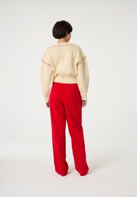 Gehaakte crèmekleurige trui met rode stikdetails, gecombineerd met hooggetailleerde rode broek. De outfit heeft een losse pasvorm en een gestructureerde stof.