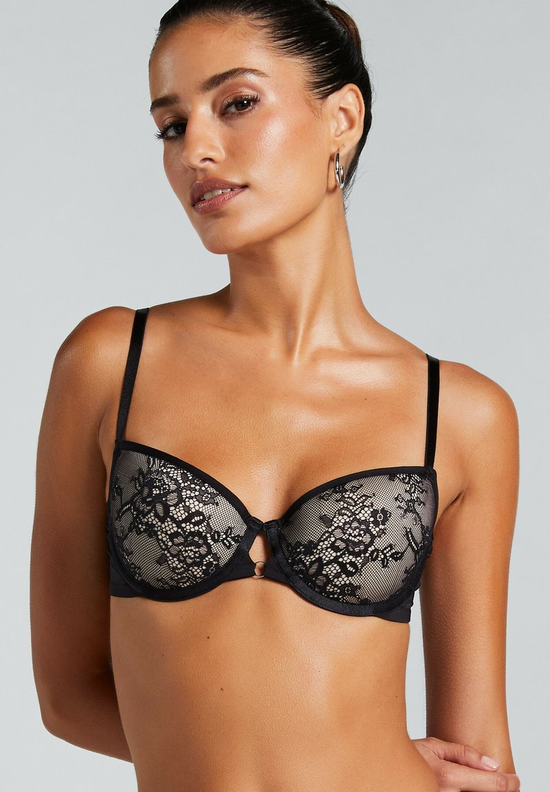 Zwarte kanten bh met beugel, doorzichtige cups met bloemmotieven, verstelbare banden en een sleutelgatdetail in het midden.