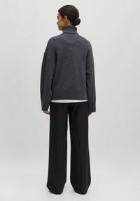 Kohlgrauer, übergroßer Rollkragenpullover mit geripptem Saum, kombiniert mit weiten schwarzen Hosen. Weiche Textur, lockere Passform, minimalistisches Design.