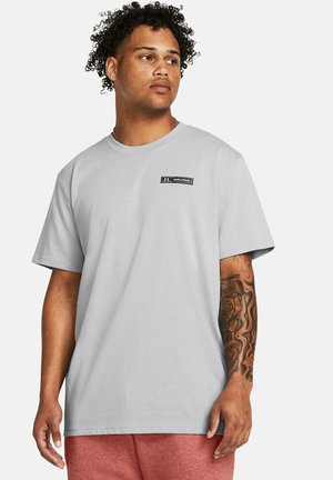 Light gray short-sleeve t-shirt with a round neckline and black logo patch detail on the left chest. Soft cotton material.