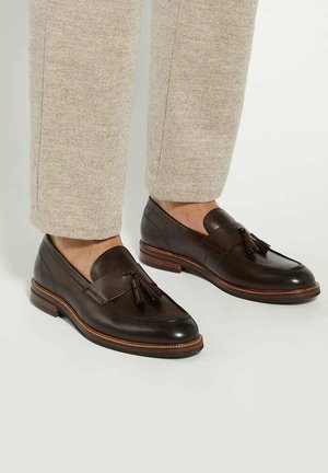 Brown leather loafers with tassel detail, smooth finish, and contrasting lighter stitching. Pairs with beige textured trousers.