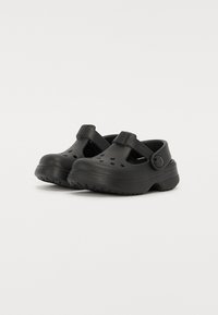 Zuecos negros con orificios de ventilación, una correa en la parte de atrás y suelas texturizadas, fabricados con material ligero y duradero. Diseño simple y funcional.