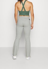 Groene sportieve crop top met kruislings rugbanden, gecombineerd met grijze uitlopende joggingbroeken. De broek heeft een subtiele textuur en een logo-label.