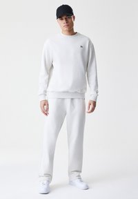 Lysegrå sweatshirt og sweatpants sæt, der har et afslappet fit, ribbede manchetter og et lille logo på brystet. Sæt med hvide sneakers og en sort kasket.