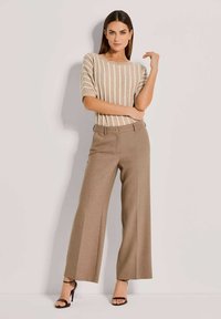 Beige gestreepte sweater met korte mouwen, gecombineerd met hoge, wijde bruine broeken. Stiletto-sandalen maken de outfit compleet.