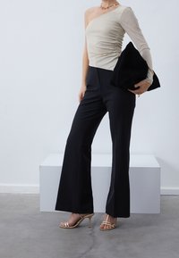 Beige one-shoulder top with ruched texture, paired with black flared trousers, and gold strappy heels; holding a black clutch with gold accents.