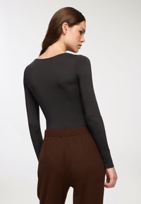 Czarny bodysuit z długim rękawem i okrągłym dekoltem, w połączeniu z brązowymi spodniami o wysokim stanie, charakteryzującymi się luźnym krojem i elastycznym paskiem w talii.