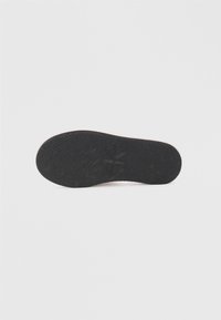 Suela de zapato de goma negra con un patrón texturizado para mayor agarre y un borde exterior rosa. Forma ligeramente redondeada en la punta.