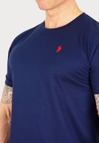 Námornícky modré bavlnené tričko s crew výstrihom, s malým červeným vyšívaným logom na hrudi. Mäkka textúra a priliehavý strih.