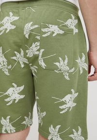 Green shorts with white leaf pattern, made of soft fabric. Features a back pocket and elastic waistband for comfort.