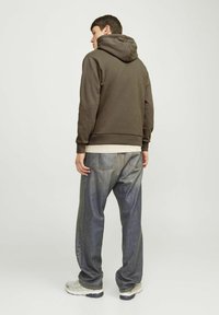 Bruine hoodie met een capuchon, gecombineerd met losse blauwe denim jeans. De stoffen zijn glad en hebben een eenvoudige uitstraling zonder zichtbare patronen.