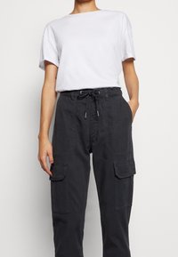 Vit bomullströja med rundad hals, kombinerad med mörkgrå cargobyxor med dragsko i midjan och sidorfickor.