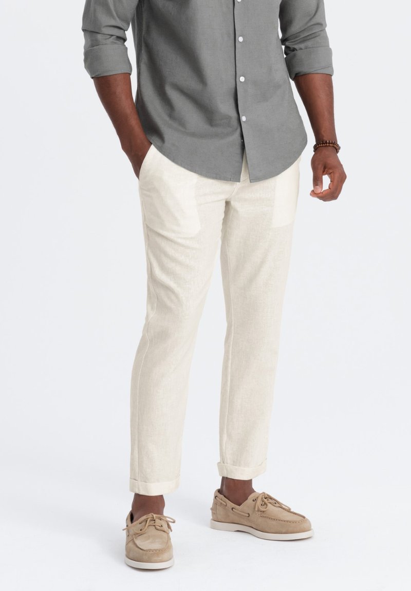 Pantalons en lin beige clair avec poches latérales et coupe droite. Associé à une chemise boutonnée grise et des chaussures marron clair.