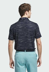 Granatowa koszulka polo z jasnymi, poziomymi wzorami, krótkimi rękawami i kołnierzykiem, zestawiona z jasnoniebieskimi spodniami. Czysta, teksturowana tkanina.