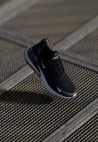 Fekete sportcipő, hálós felsőrésszel, kerek orral, Nike logóval és látható légpárnázó egységgel. Texturált talp rácsszerű felületen.