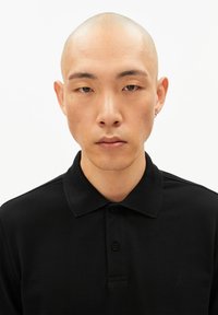 Schwarzes Poloshirt mit Kragen, strukturierter Stoff und Logodetail auf der linken Seite. Könnte zwei Knöpfe am Kragen haben.