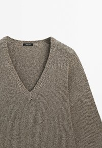 Pull à col en V en maille marron clair. Présente un motif texturé et une coupe ample avec des épaules tombantes. L'étiquette indique "Massimo Dutti."
