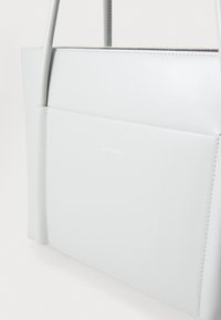 Borsa tote in pelle grigia chiara di Calvin Klein con texture liscia, design strutturato e tasca esterna. Presenta cuciture minimaliste e branding.