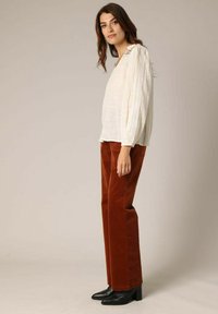 Witte textuurblouse met lange mouwen, gecombineerd met roestkleurige corduroy broek en zwarte leren enkellaarzen met hak.