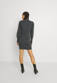 Vestido de suéter gris acanalado con una silueta ajustada, mangas largas abullonadas y un cuello alto, combinado con botas de tobillo negras de tacón.